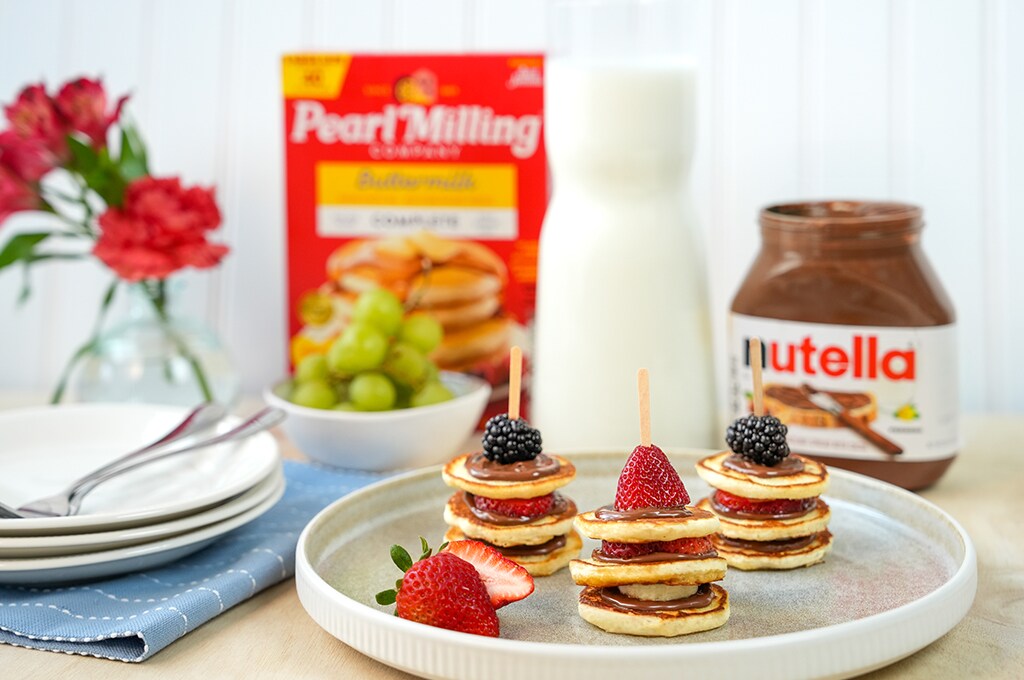 Mini Pancake Stack with Nutella®, berries on a plate, half-cut strawberry, some grapes, Nutella® jar and Pearl Milling Company pancake mix in the background.