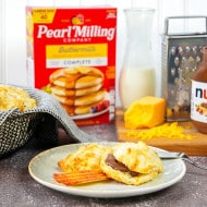 Apple Cheddar Biscuits with Nutella® and cut apples on a plate, Nutella® jar, cheese, more cheese biscuits and Pearl Milling Company buttermilk pancake mix are placed in the background.