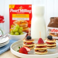 Mini Pancake Stack with Nutella®, berries on a plate, half-cut strawberry, some grapes, Nutella® jar and Pearl Milling Company pancake mix in the background.