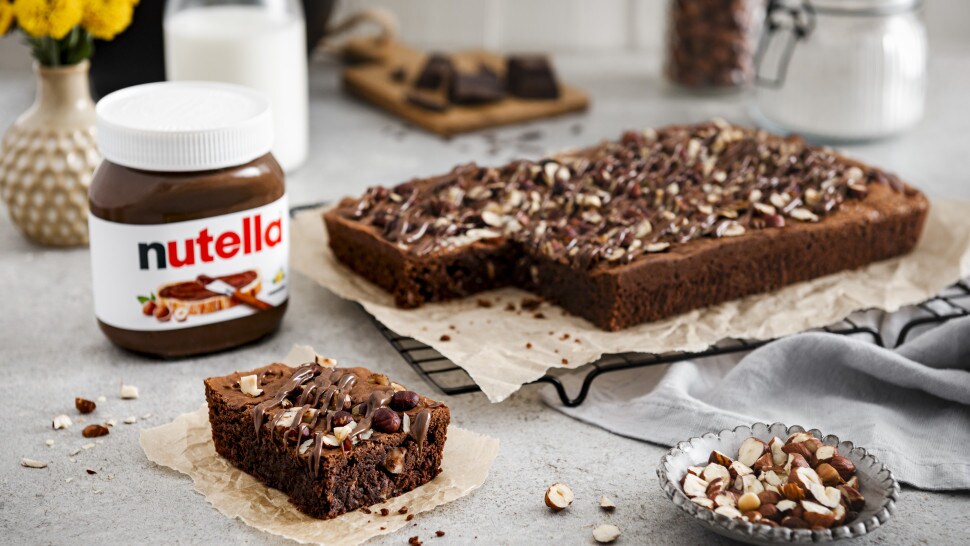 The Nutella® brownie is placed on a cooling rack lined with parchment paper. A square has been cut from the brownie and placed next to a jar of Nutella®.