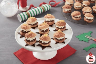 Eight cream puffs, filled with cream and Nutella® are displayed on a white cake stand. Extra Nutella® cream puffs sit in the background.