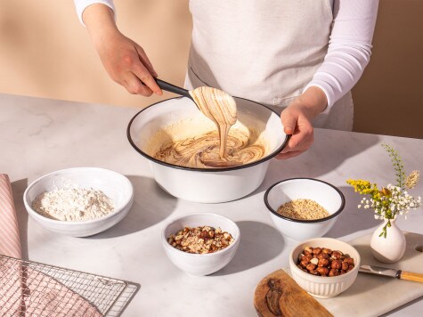 A baker stirs melted chocolate into the brownie mixture using a spoon.