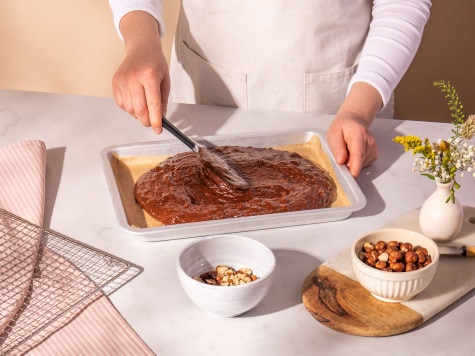 A baker spreads brownie batter into a baking sheet in preparation for baking.