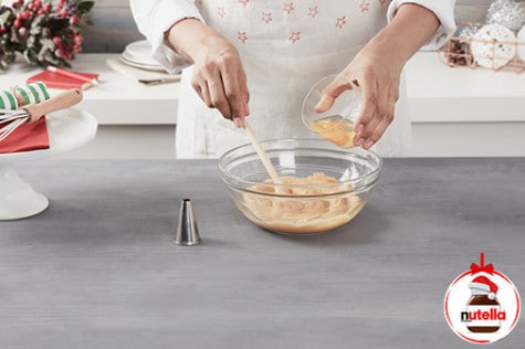 In a large glass bowl, a baker whisks together eggs and the choux pastry mixture.
