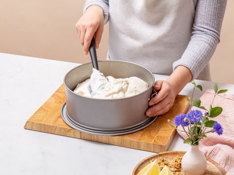 A baker is placing the no bake cheesecake filling on top of the crumb bottom in the springform pan.
