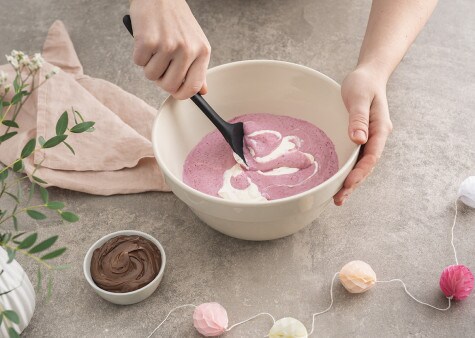 Cream is being mixed together with a berry puree in a large mixing bowl by a wooden spoon.