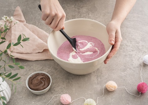 Cream is being mixed together with a berry puree in a large mixing bowl by a wooden spoon.