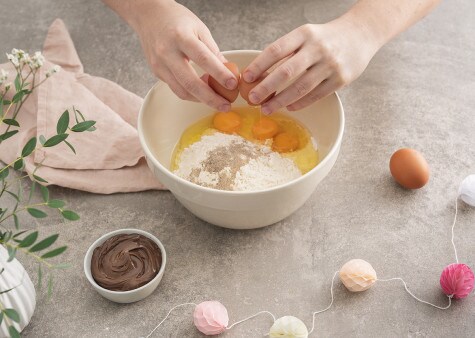 Eggs are being cracked into a large mixing bowl, which also contains flour and sugar to make a crepe mixture.