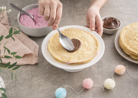 Nutella® is being spread onto a crepe base to layer the crepes into a cake.